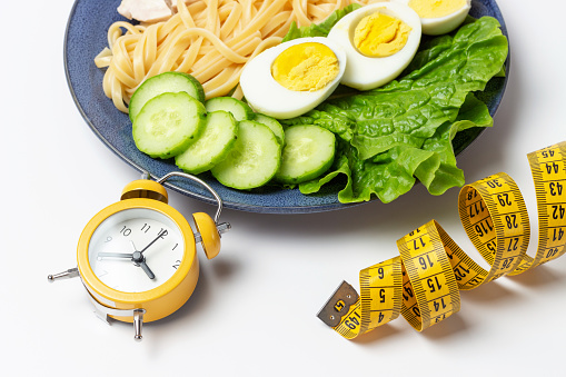 Plate with food on a white background and alarm clock, a interval fasting concept