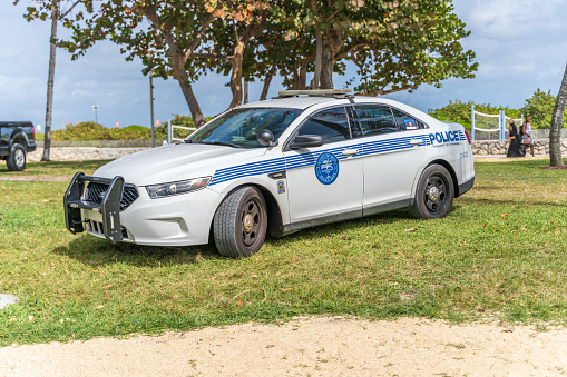 Miami police car parked on grass verge at Miami Beach. Two people walking by in the background