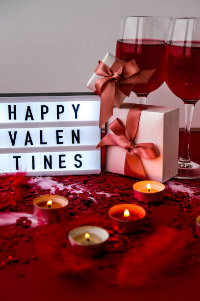 istock Lightbox with text HAPPY VALENTINES two glasses of red wine and gift boxes Burning red candles on confetti sequinned background with feathers. Saint Valentines Day and Christmas background 1294794655
