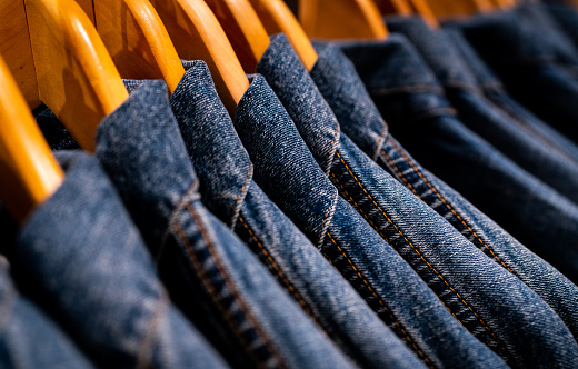 Selective focus on jacket jeans hanging on rack in clothes shop. Denim jeans with jeans pattern. Textile industry. Jeans fashion and shopping concept. Clothing concept. Denim jacket on rack for sale.