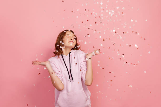 Extremely happy young brunette female enjoying falling heart shaped confetti and smiling with closed eyes, celebrating valentines day, holiday mood Extremely happy young brunette female enjoying falling heart shaped confetti and smiling with closed eyes, celebrating valentines day, holiday mood. Indoor studio shot, isolated on pink background 14 15 years photos stock pictures, royalty-free photos & images