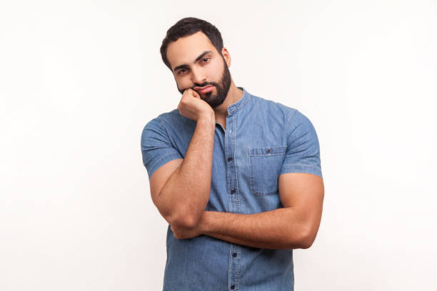 istock Bored upset man with beard in blue shirt leaning head on hand looking at camera with indifferent look, laziness and apathy, procrastination 1294803729