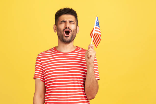 engagierter patriotischer mann in gestreiftem t-shirt hält in der hand flagge der vereinigten staaten von amerika, singen hymne feiert unabhängigkeitstag - hispanic male stock-fotos und bilder