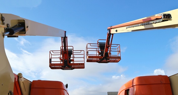Back view of two aerial work platforms against blue sky with clouds. No people.