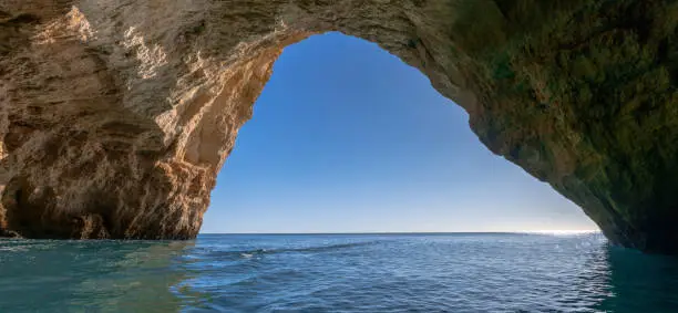 A panorama view from inside a cave on the ocean coast with turquoise water and sunny blue sky outside