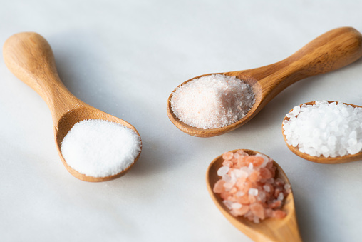 Various salt types in 4 wooden spoons on white marble.