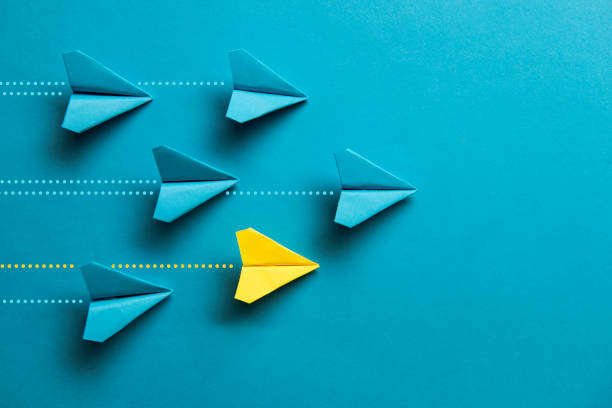 Individuality ONe yellow paper plane is flying on blue background among  a group of blue paper planes. Representing individuality. paper airplane photos stock pictures, royalty-free photos & images