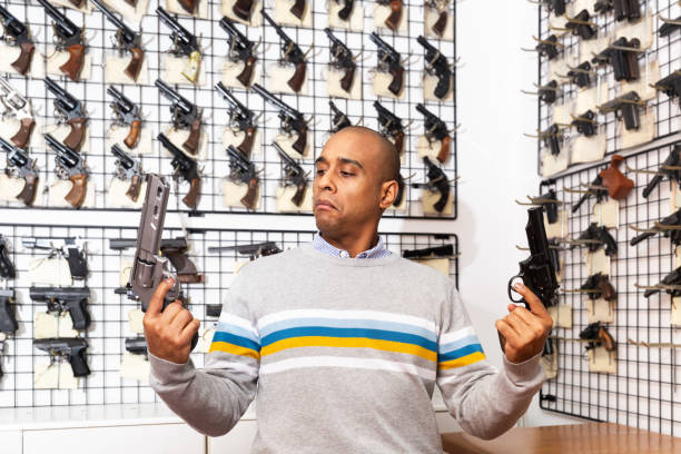 istock Surprised hispanic man comparing two handguns in gun shop 1294817295