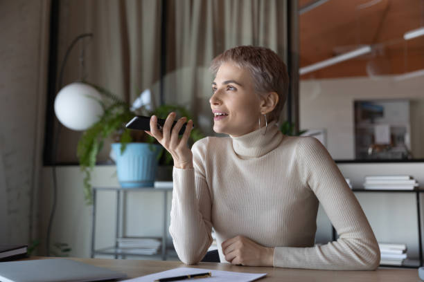 smiling businesswoman recording voice message on phone in office - conference phone imagens e fotografias de stock