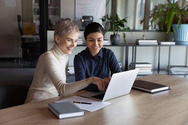 istock Smiling diverse colleagues using laptop together, chatting, discussing project 1294818709