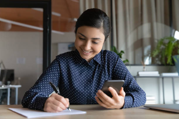 istock Smiling Indian woman writing notes, watching webinar on phone 1294818786