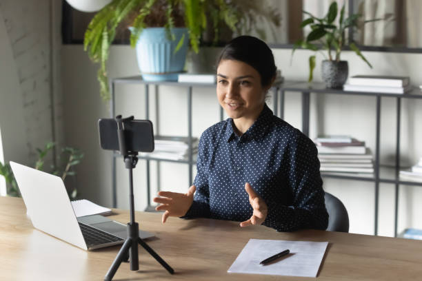 Successful Indian businesswoman recording webinar, using smartphone on tripod