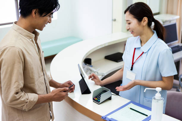 ein mann, der mit dem smartphone in einem krankenhaus bezahlt - healthcare and medicine receptionist paying credit card stock-fotos und bilder