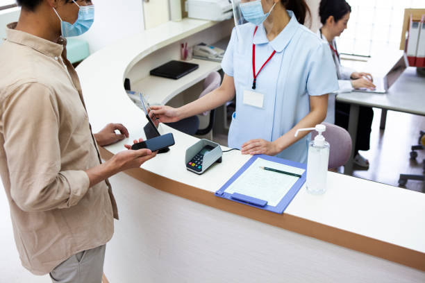 ein mann, der mit dem smartphone in einem krankenhaus bezahlt - healthcare and medicine receptionist paying credit card stock-fotos und bilder