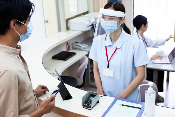 ein mann, der mit dem smartphone in einem krankenhaus bezahlt - healthcare and medicine receptionist paying credit card stock-fotos und bilder