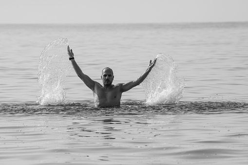 Middle Eastern man is standing in the sea and creating a water splash with his hands