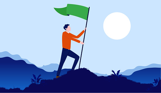 Male person celebrating life goals and victory by raising green flag on hilltop with landscape and sun in background.