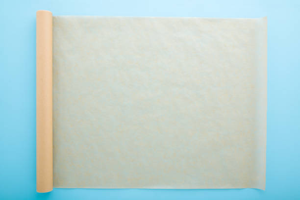 istock Rolled out roll of baking paper on light blue table background. Pastel color. Closeup. Top down view. Empty place for text. 1294825748