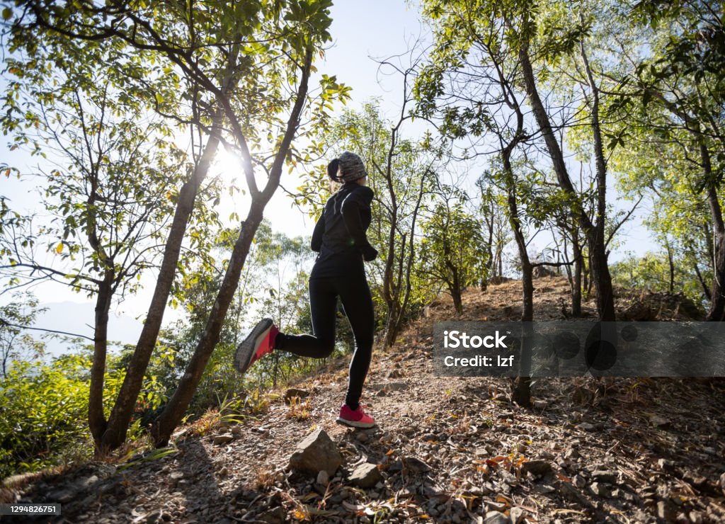 Fitness asian woman running on trail at sunrise tropical forest in winter Cross-Country Running Stock Photo