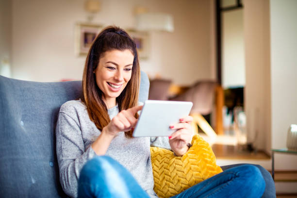 istock Happy woman using digital tablet while sitting in the armchair at home 1294834840