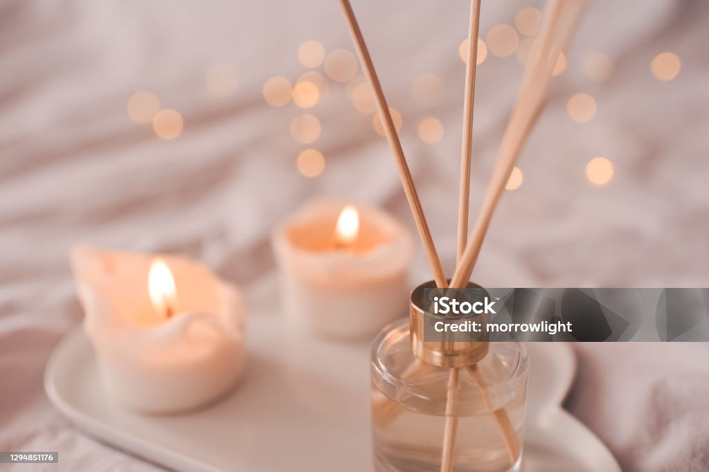 Cozy home atmosphere Home aroma fragrance diffuser with burning candles on white tray in bed over glowing lights close up. Cozy atmosphere. Wellness. Healthy lifestyle. Candle Stock Photo