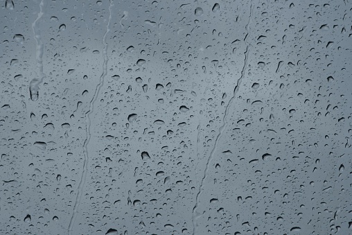 Raindrops on the window during daytime and grey sky background