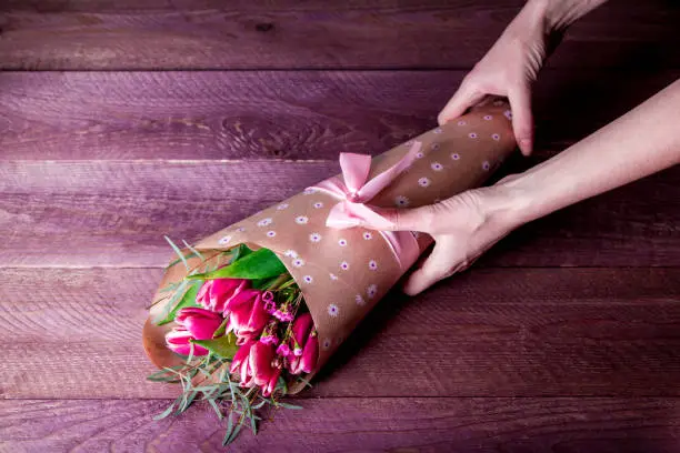 Photo of florist makes a bouquet with tulips in Kraft paper