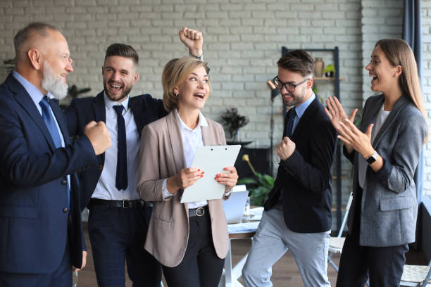 istock Happy modern business people are keeping arms raised and expressing joyful while standing in office. 1294870291