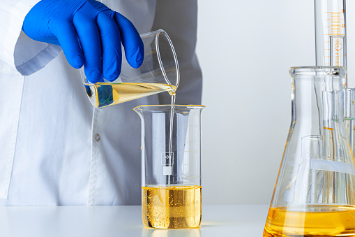 Scientist or doctor in blue gloves pouring some yellow liquid into a flask close up