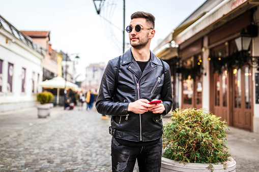 Young caucasian man using phone while walking through the city