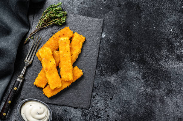 istock Oven baked crumbed fish sticks made from white fish.  Black background. Top view. Copy space 1294877184