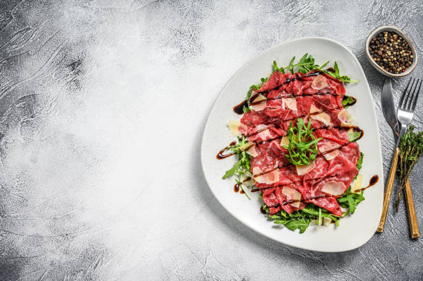 Italian Beef carpaccio with arugula salad, parmesan cheese. Gray background. Top view. Copy space Italian Beef carpaccio with arugula salad, parmesan cheese. Gray background. Top view. Copy space. carpaccio parmesan cheese beef raw stock pictures, royalty-free photos & images