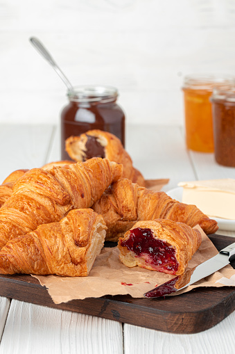 Fresh croissants with berry jam on dark wooden board, close up