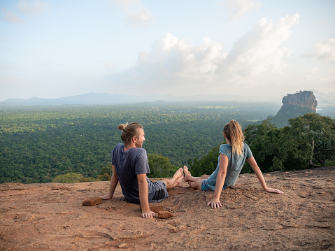 Rear view of young couple sitting on top of rock at sunset contemplating the beautiful jungle natural landscape. People travel relaxation