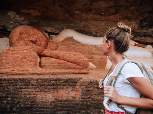 istock Young woman contemplates Buddha statue in rock 1294882163