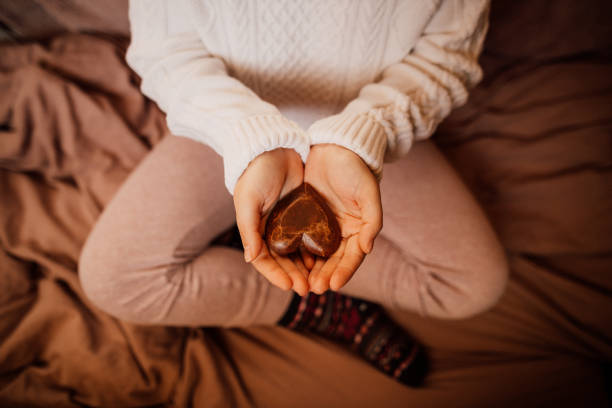 istock Unrecognizable young woman in cozy woolen socks and pullover with winter blankets holding a wooden heart in her hands 1294884582