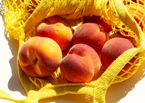 istock Close-up Ripe peaches in a mesh bag or string bag on light yellow background. Flat lay. Zero waste. 1294885619