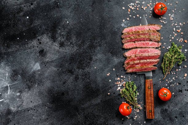 istock Grilled and sliced flat iron rare steak. Marble beef meat. Black background. Top view. Copy space 1294885828