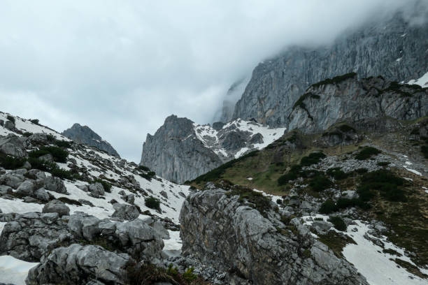 A panoramic view on the Alpine peaks in Austria from Marstein. The slopes are mostly covered with snow. Stony and sharp mountains. Overcast. Baren slopes, green valley below. Serenity and calmness