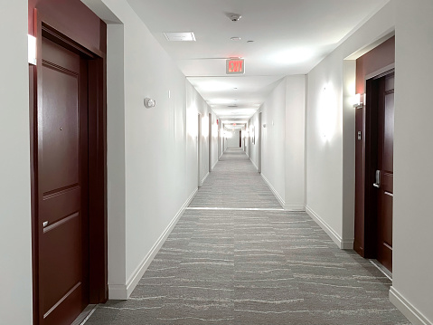 Picture of long corridor with clean marble floor, many closed doors along side, bright lighting and brown doors