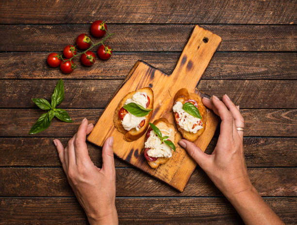 istock Homemade bruschettas with stracciatella cheese cherry tomatoes and basil on wooden cutting board. Woman hands making bruscettas. 1294890665