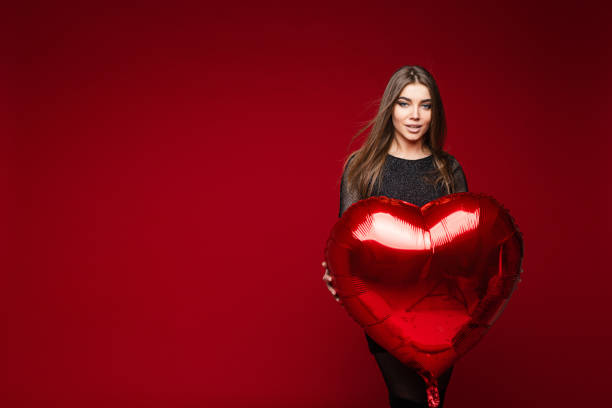 istock Pretty young elegant woman posing and holding red balloon in studio 1294893000