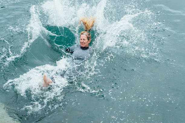 Confident and Courageous A mature woman about to be submerged into the sea after jumping in backwards. She is in Cornwall. woman cold water swimming stock pictures, royalty-free photos & images