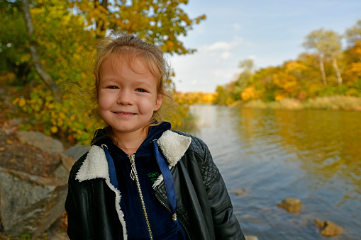 A little girl walks in the autumn forest, plays and throws pebbles into the river.