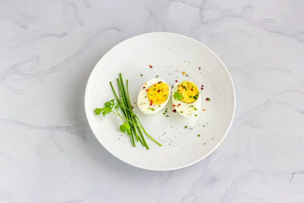 Boiled Eggs on a White Dish Garnished with Black Pepper, Chili Flakes, Salt and Chives Directly Above  Photo