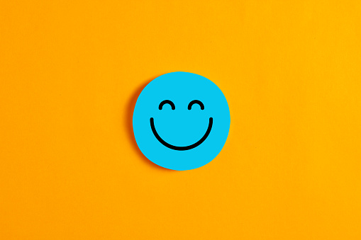 Blue round circle with a happy or smiley face icon on it against yellow background. Positive expression or customer satisfaction in business concept.