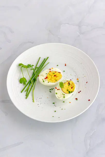 Boiled Eggs on a White Dish Garnished with Black Pepper, Chili Flakes, Salt and Chives Directly Above  Photo