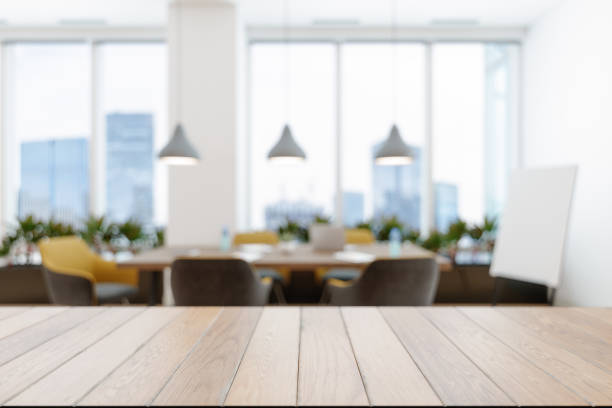 superficie vuota in legno e sala riunioni sfocata astratta con tavolo da conferenza, sedie gialle e piante. - ufficio foto e immagini stock