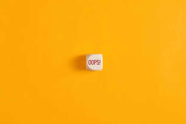 Photo of Oops sign on wooden cube over yellow background.
