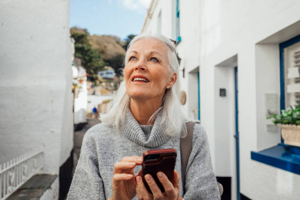 Looking for a Specific Street A senior woman looking up while walking around and exploring the streets of Polperro, Cornwall. She is using maps on her mobile phone to follow directions around the village. fishing village photos stock pictures, royalty-free photos & images